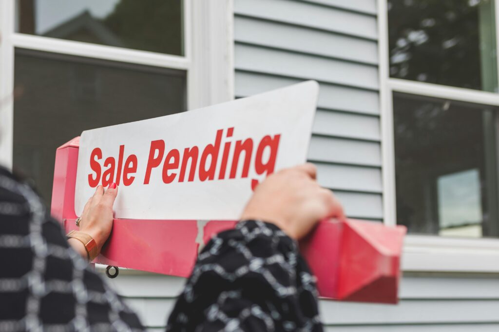 a picture of a real estate agent placing a Sale Pending sign outside of a home.